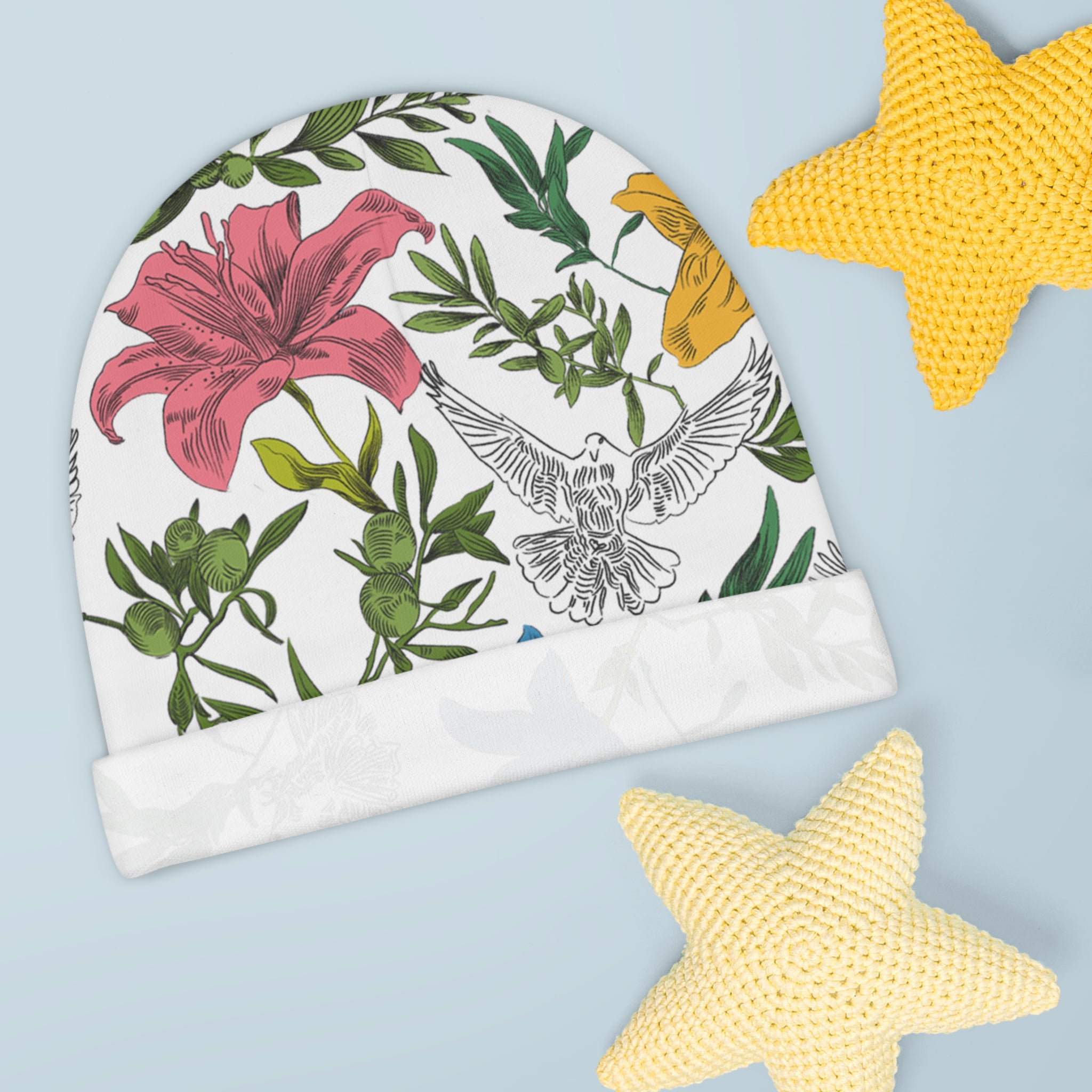 Baby beanie with floral and dove design on a light blue background with yellow knitted stars.