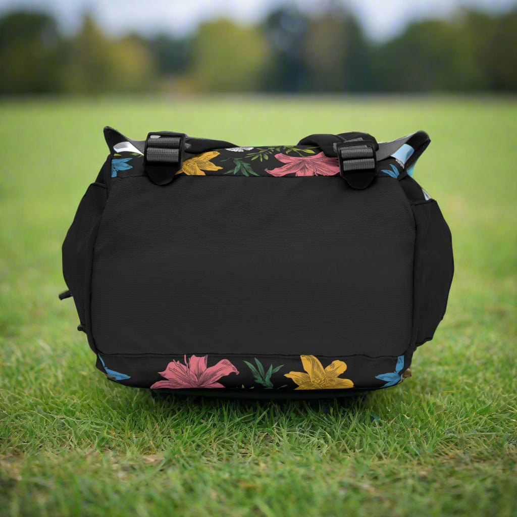 Bottom view of a floral backpack with adjustable straps laying on the grass in a park