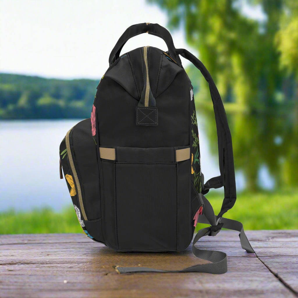 Left side of floral-patterened backpack sitting on a table against an open park background with a lake