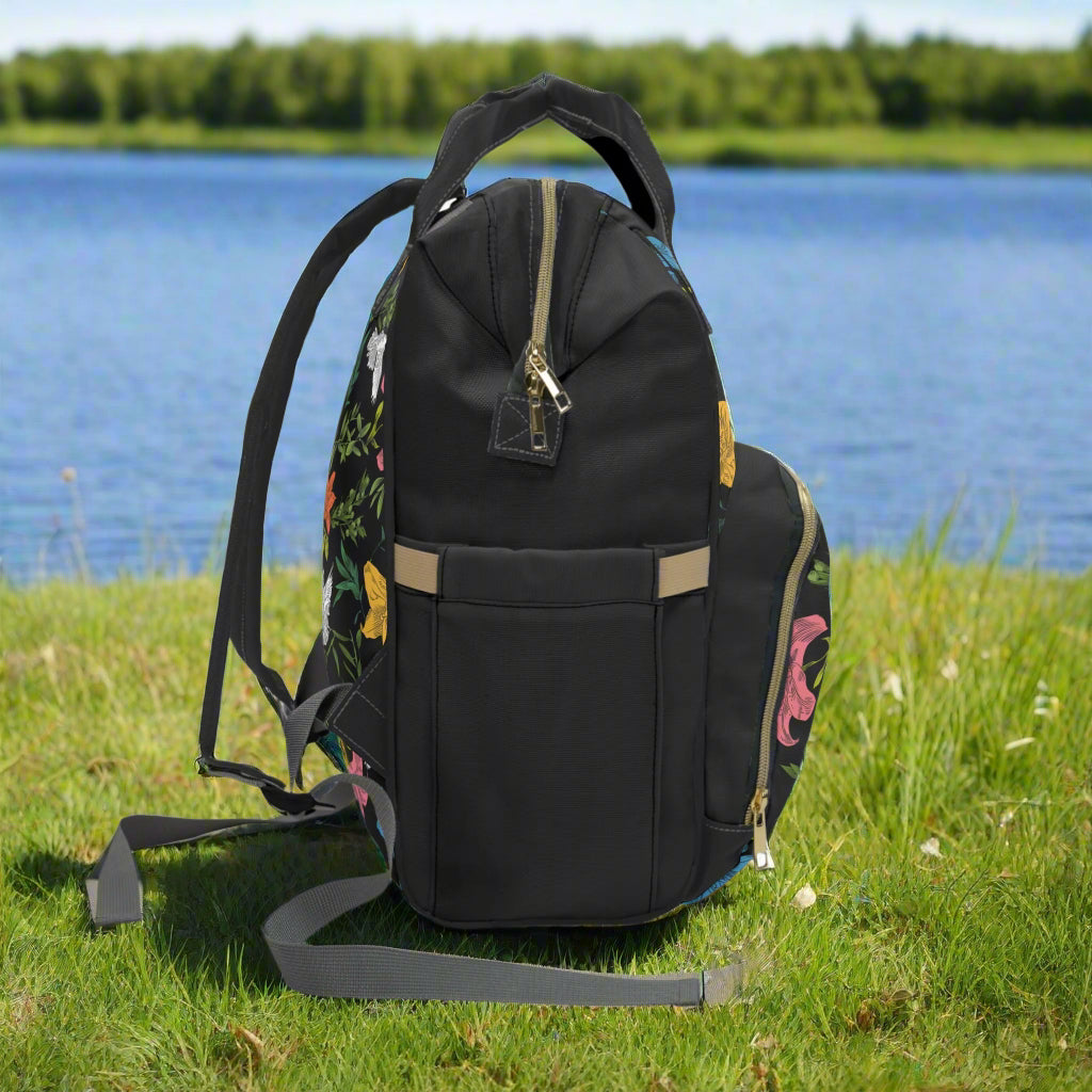 Right side of floral backpack on the grass next to a lake on a sunny day
