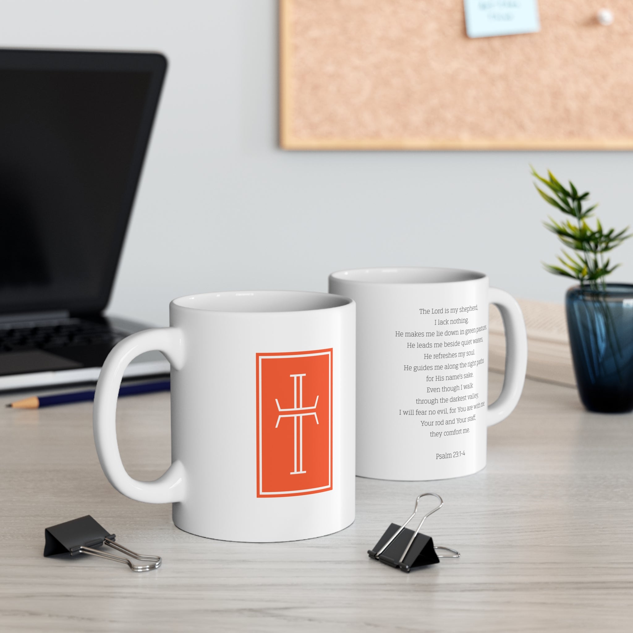 Two white mugs with a white cross and vibrant umber of sardius background on the front, and  the Biblical verse Psalm 23:1-4 on the back. The mugs are sitting on a desk with office supplies.