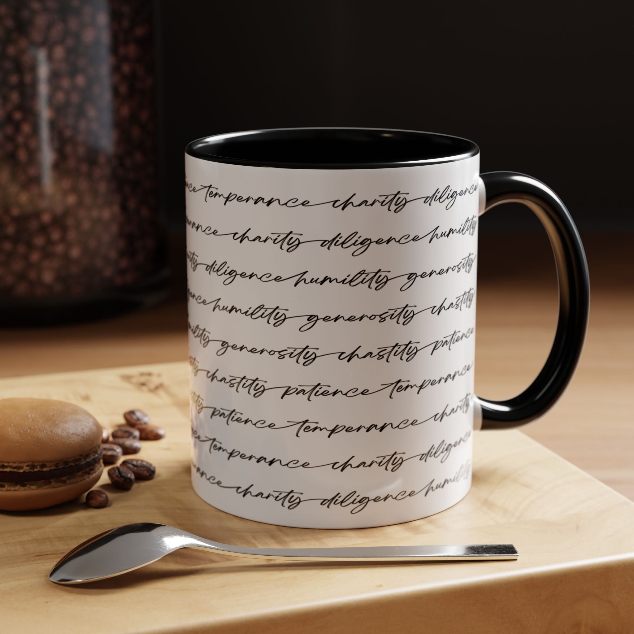 White mug with the seven virtues scripted along the outside, with black interior and handle on a wooden surface with coffee beans and a spoon.