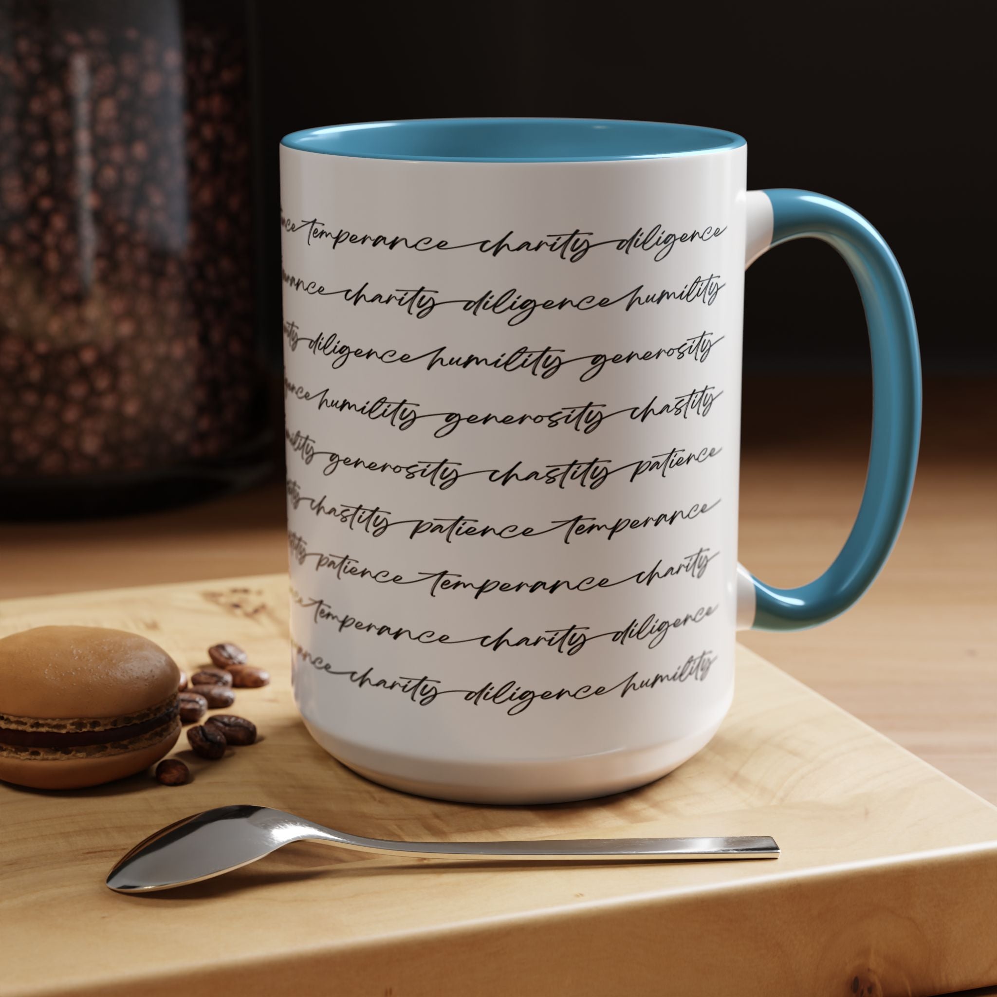 White mug with the seven virtues scripted along the outside, with blue interior and handle on a wooden surface with coffee beans and a spoon.