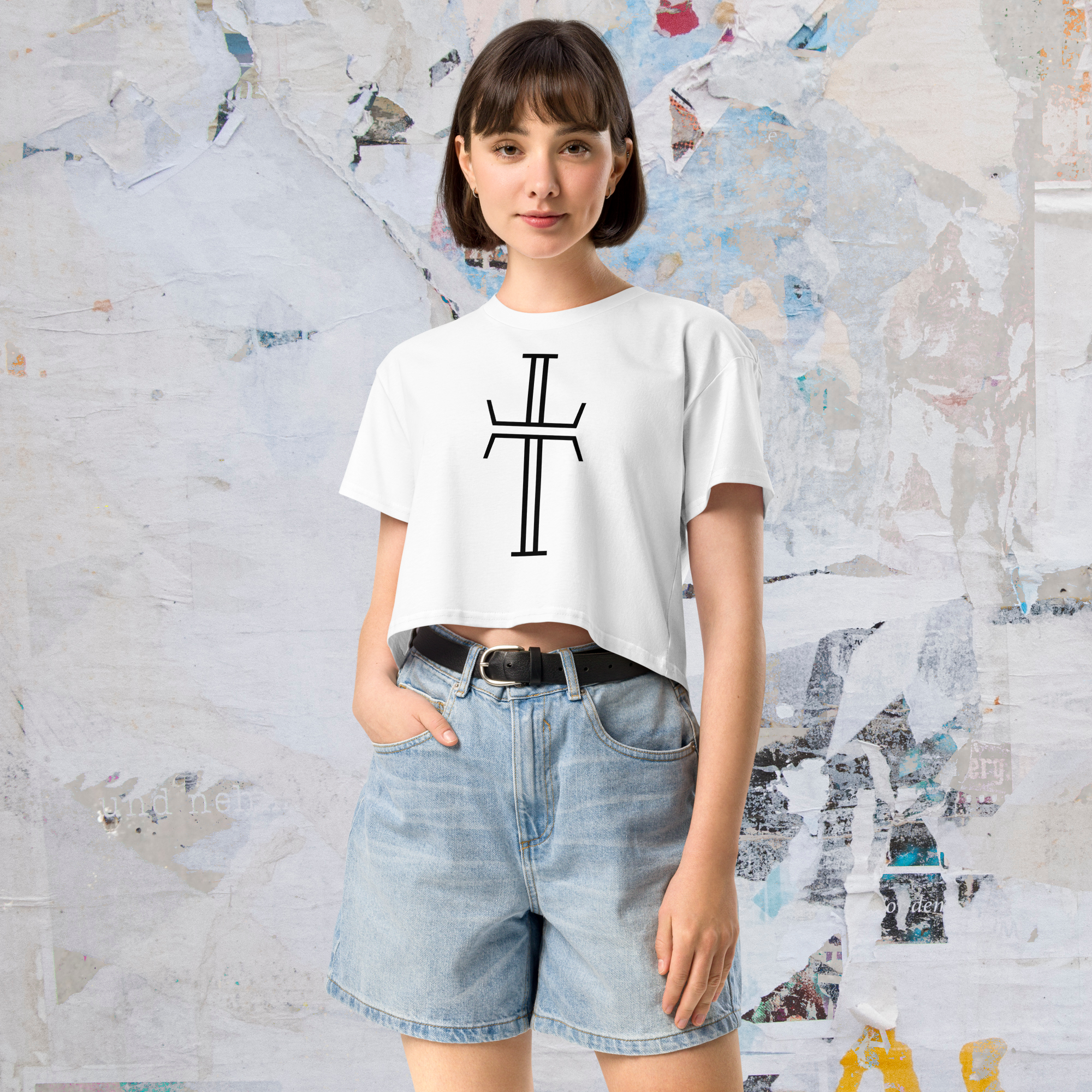 The front angle of a female model wearing jean shorts and a cropped white tee shirt that has a large Purpose cross logo in black ink, centered across the front.