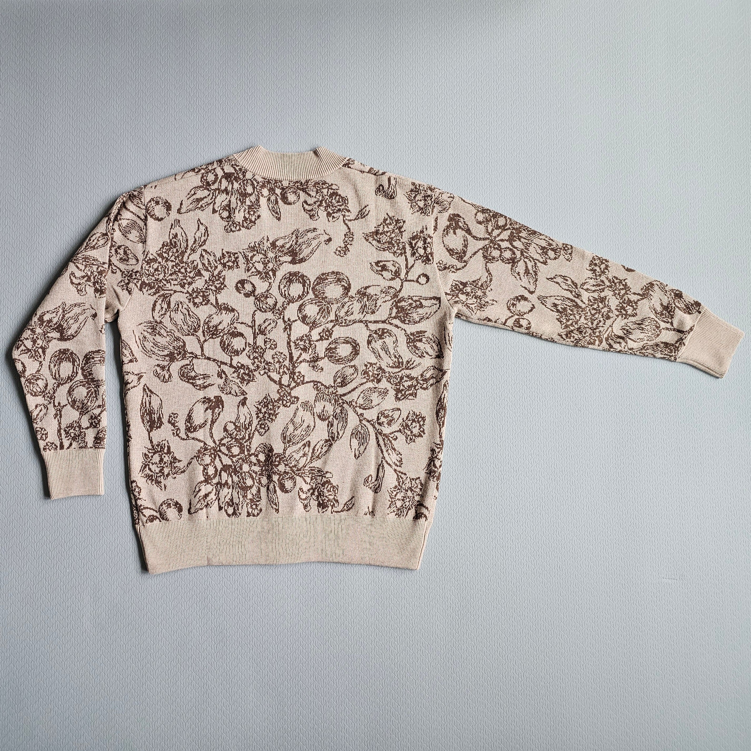 Back view of a beige sweater with black floral pattern on a gray background
