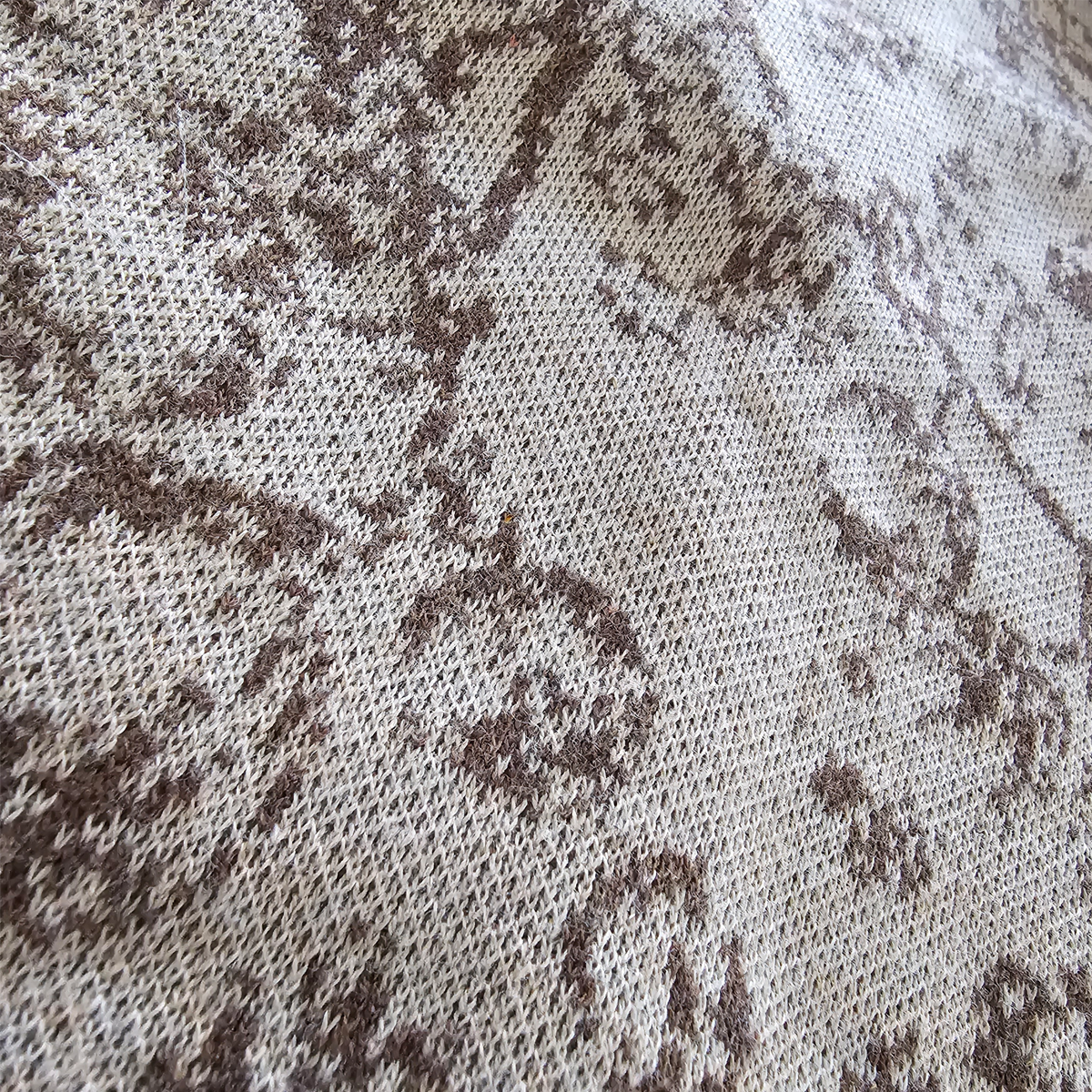 An angled close-up of the brown knitted floral pattern on the beige sweater.