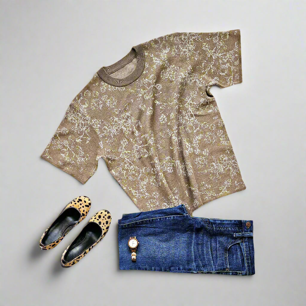 A brown knitted tee with a floral pattern, displayed flat with a pair of blue jeans, leopard-print flats, and a watch.