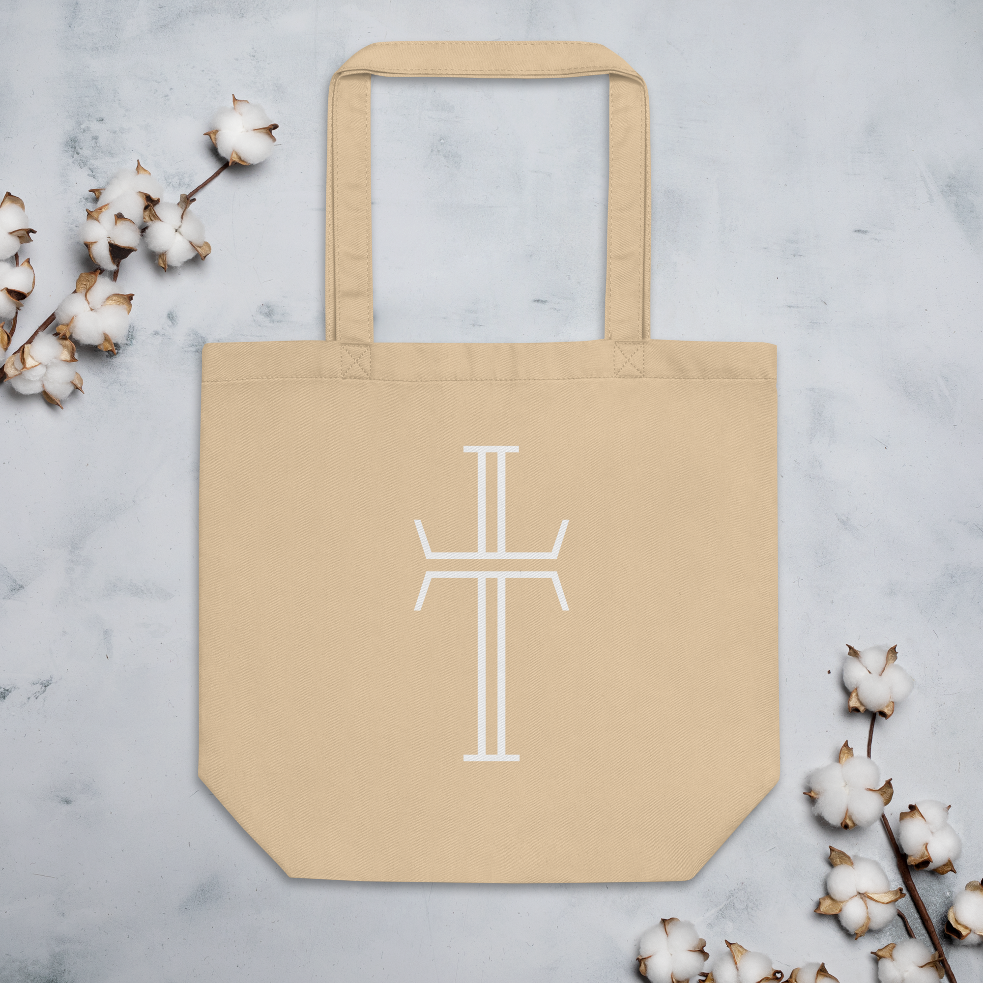 Cream-colored tote bag laying flat, with the white Purpose cross logo on the front of the bag. The bag has long, generous handles.