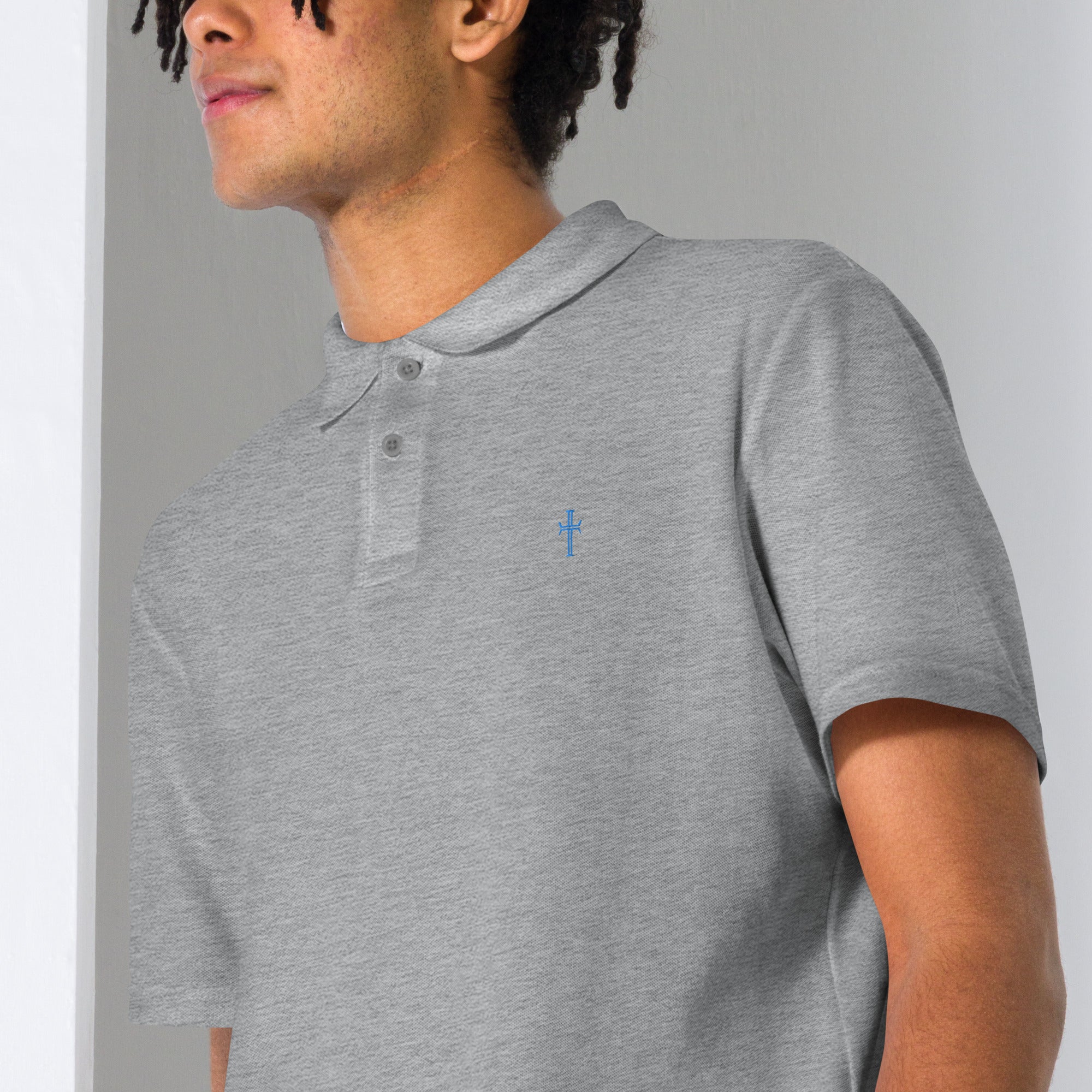 Close up of a male model wearing a gray pique knit polo with the Purpose cross logo in blue thread embroidered on the left chest area.