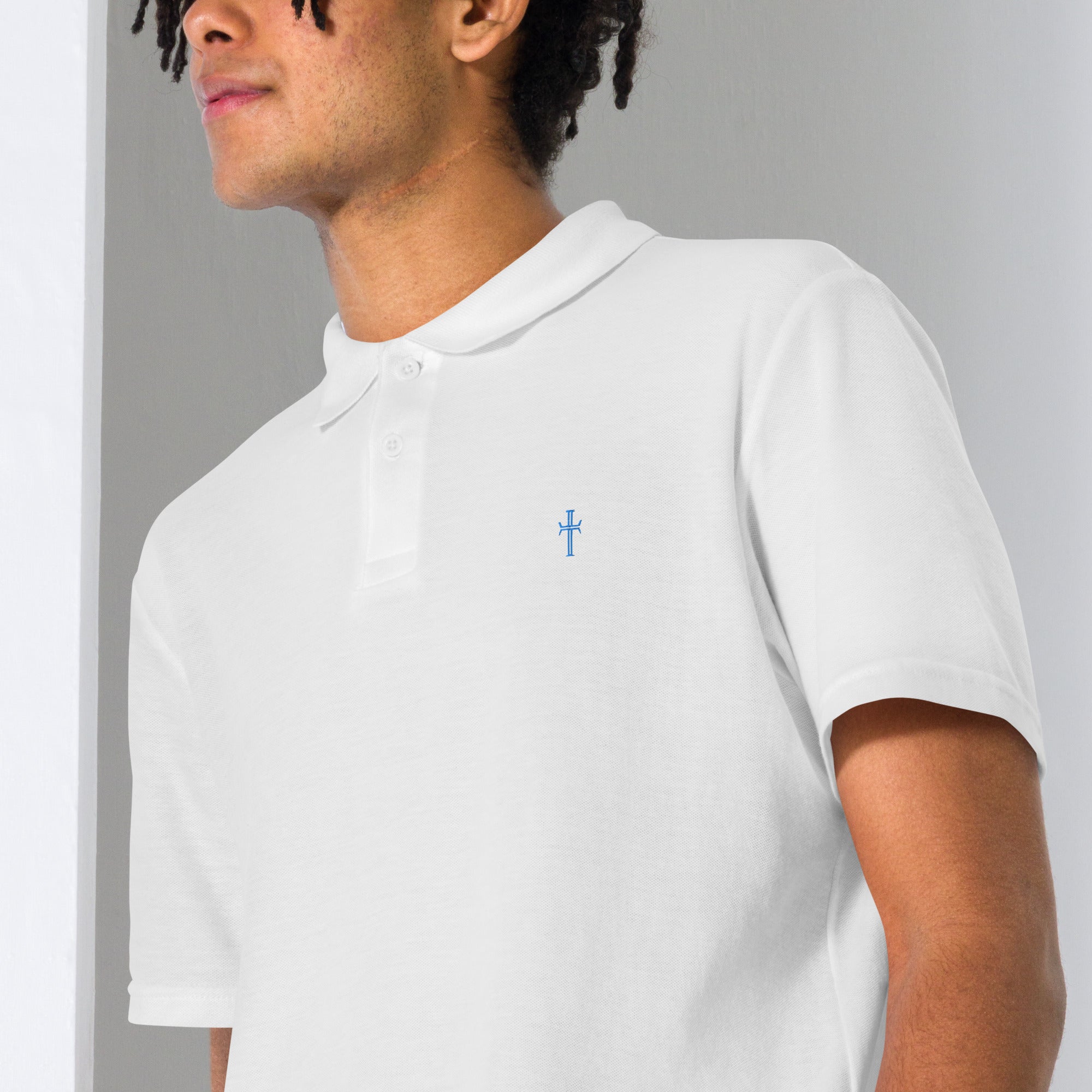 Close up of a male model wearing a white pique knit polo with the Purpose cross logo in blue thread embroidered on the left chest area.