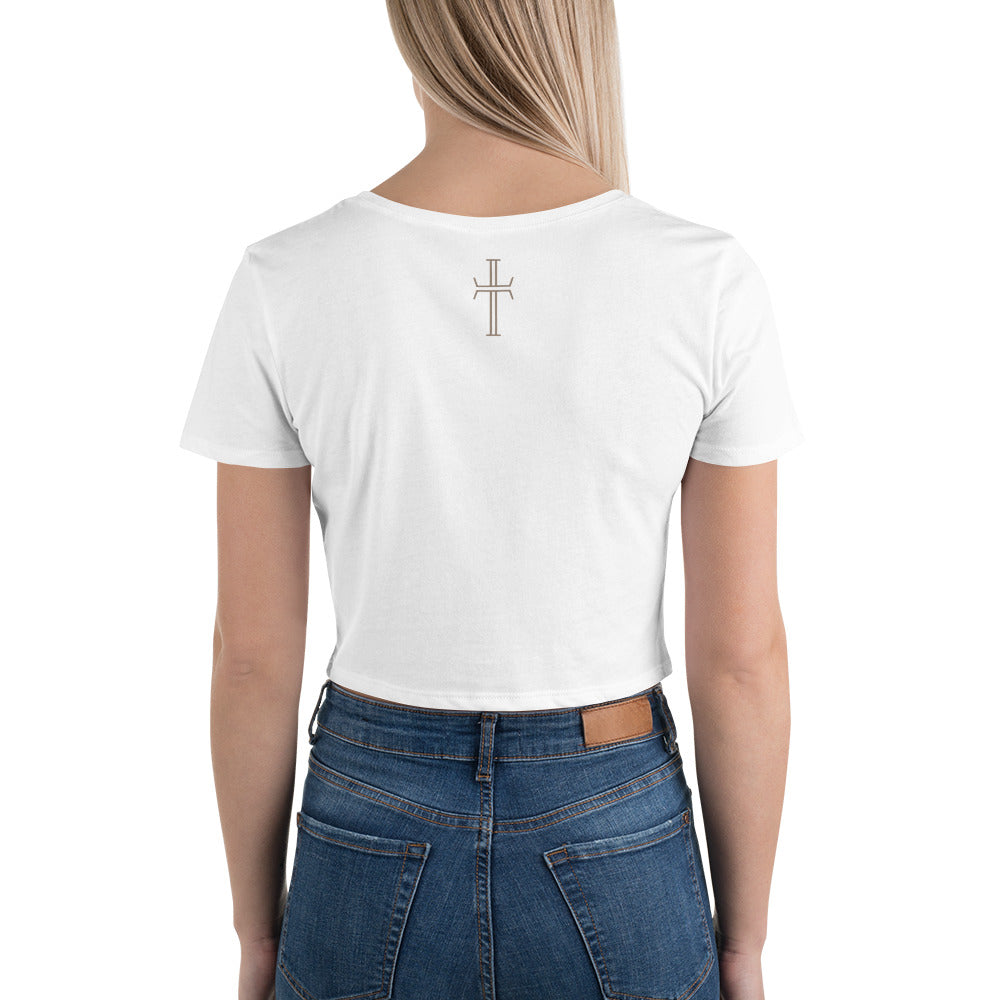 The back upper half of a female model is wearing a white, cropped tee shirt with a beige cross on the upper center of the shirt back.