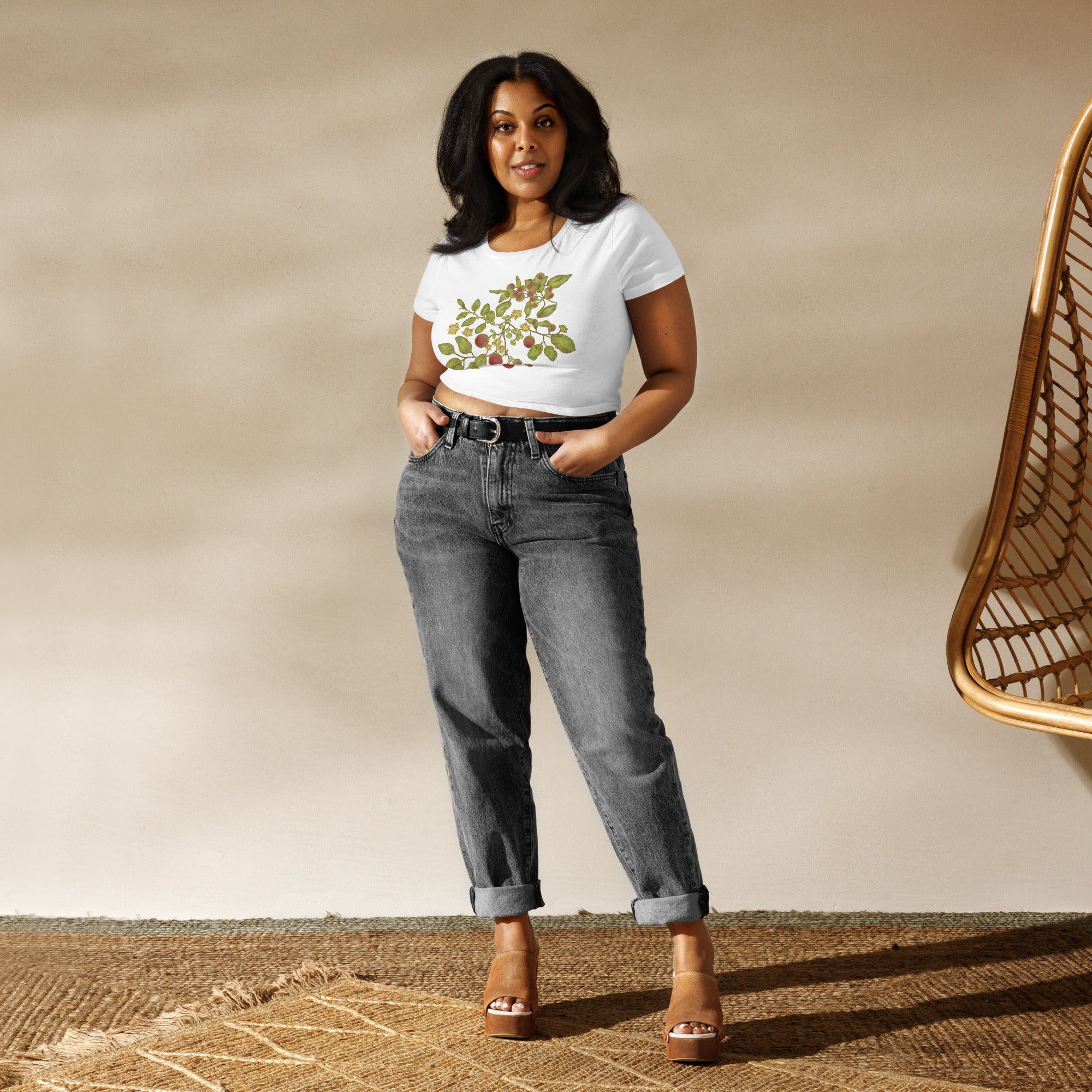 A female model wears a pair of loose-fitting, black, faded and cuffed jeans, with high leather wedges, and a white cropped tee shirt with a floral image of a plant with various green, red, and yellow tones.